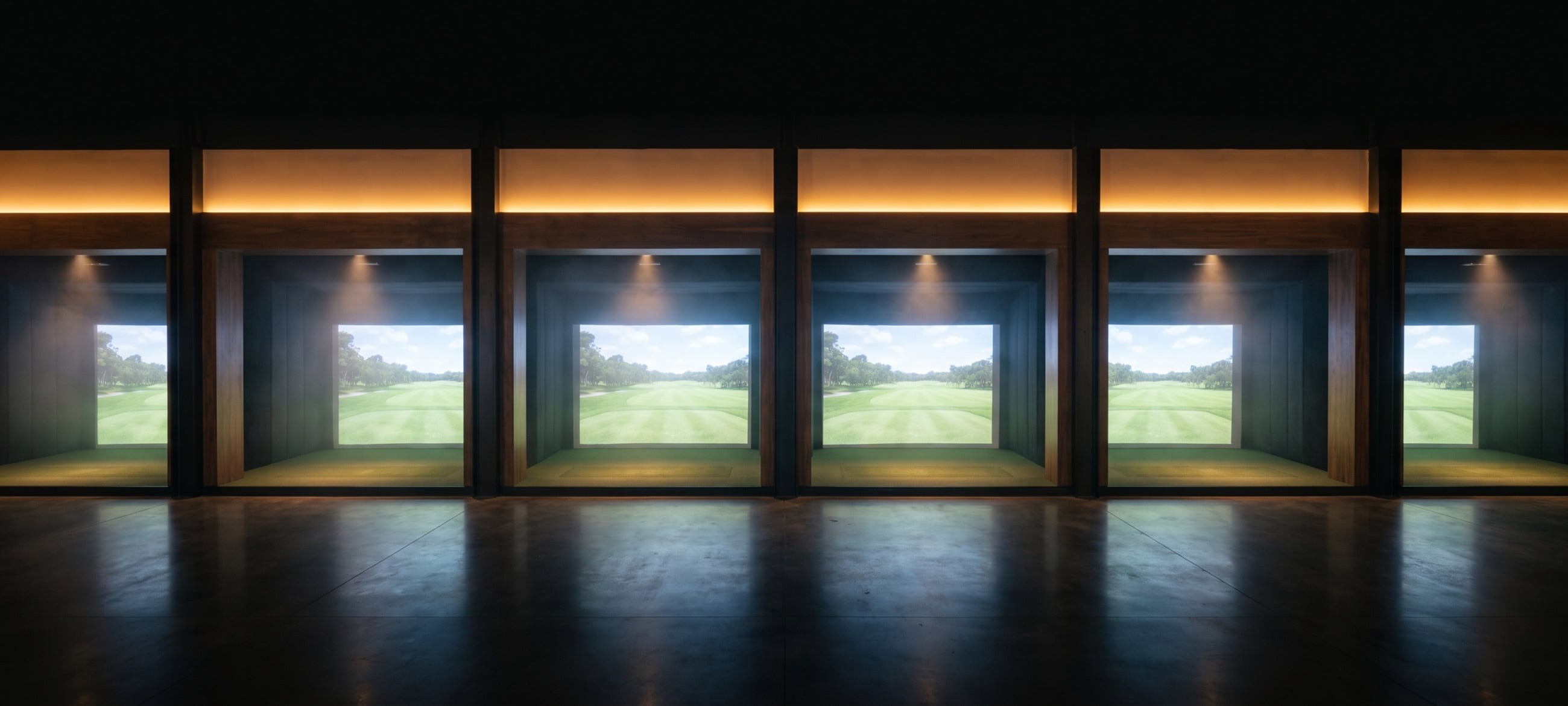A row of six identical indoor golf simulator bays, each lit by its own screen.