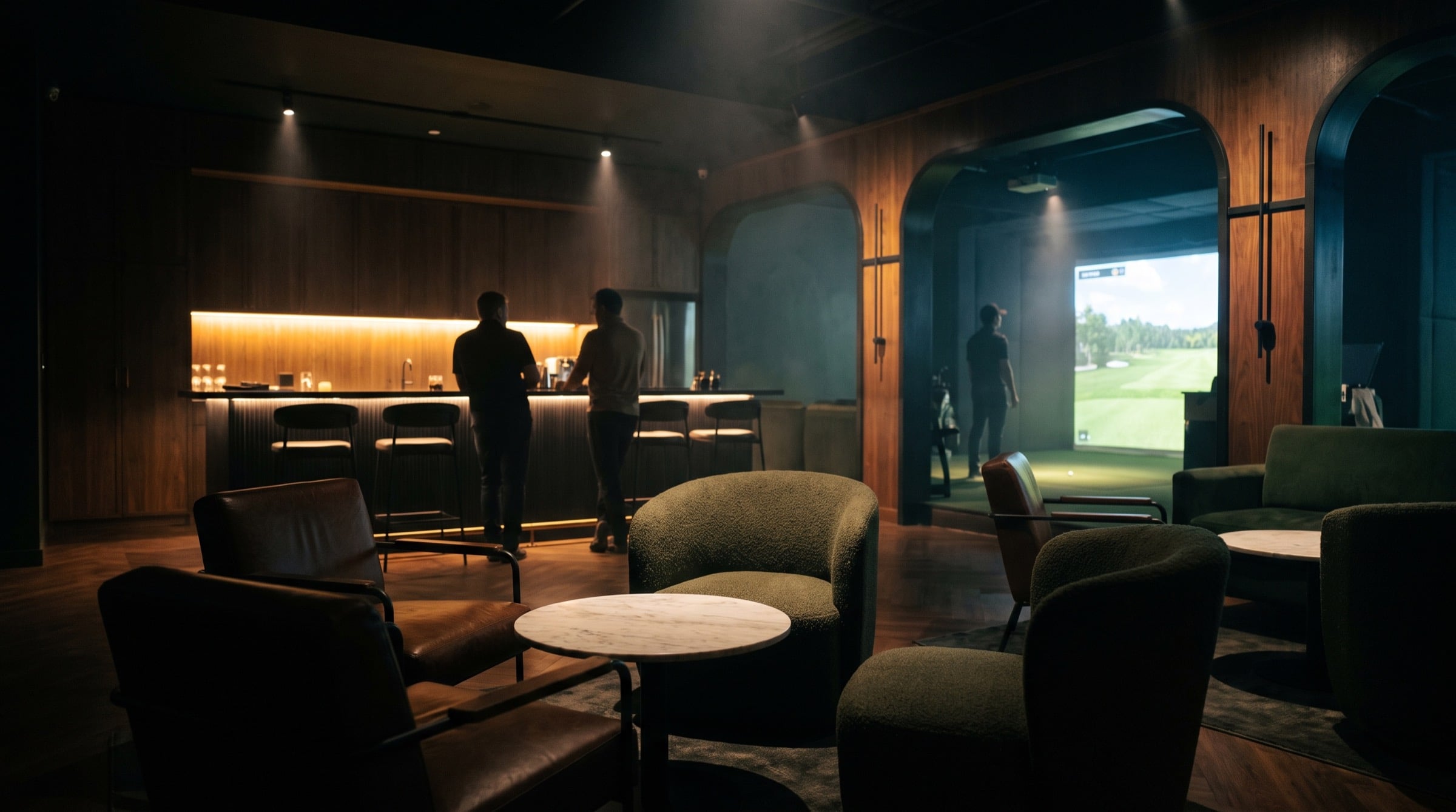 A lounge with low seating and a bar beside an indoor golf simulator bay.