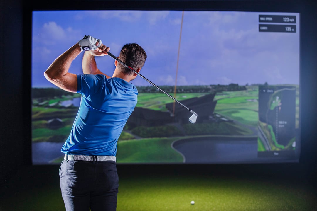 A golfer facing a large screen showing a rendered golf course.